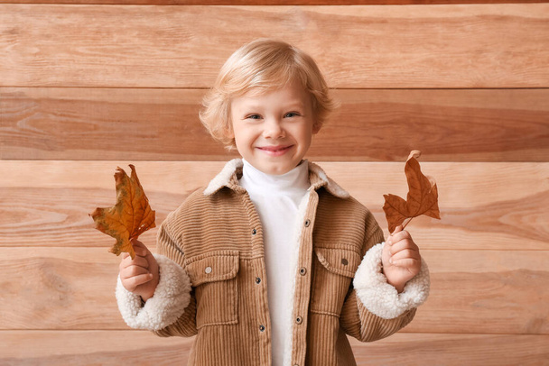 Cute little boy with autumn leaves on wooden background - Photo, Image