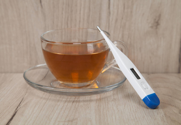 Medizinisches Thermometer und Tee isoliert auf Holzgrund. - Foto, Bild