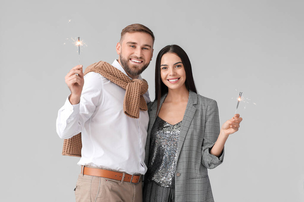 Young couple with Christmas sparklers on grey background - Photo, Image