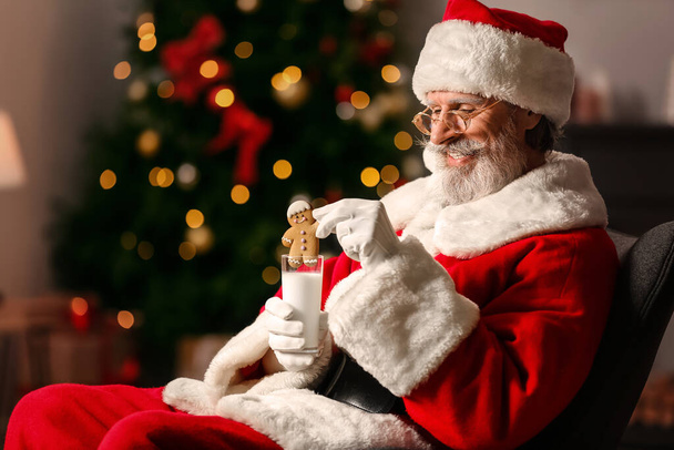 Santa Claus with tasty gingerbread cookie and milk at home - Photo, Image