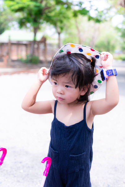 Adorável menina asiática está vestindo um chapéu branco com bolinhas em muitas cores. As crianças usam chapéus para protegê-los do sol quente durante o dia. A criança está vestida de preto, tem 3 anos. - Foto, Imagem