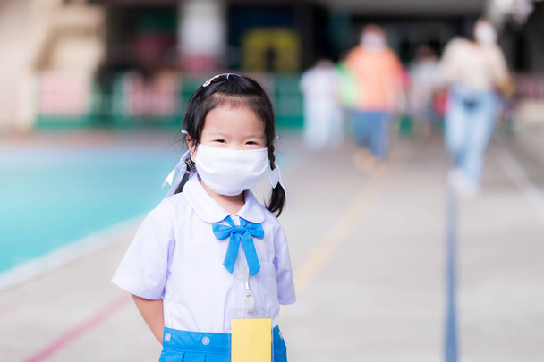 Азійська дівчинка в білій масці, щоб захистити від вірусу. Вона носила шкільну форму, синю спідницю, що стояла на цементному полі. Концепція: діти повертаються до школи з вірусом корони.. - Фото, зображення