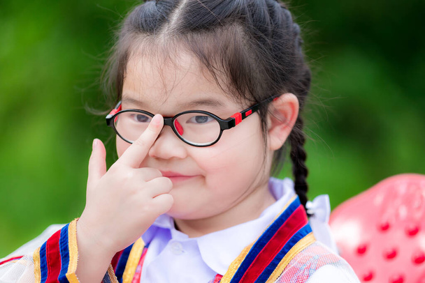 Strzał w głowę słodkich dzieci noszą okulary z powodu krótkowzroczności lub lekkiego astygmatyzmu. Dzieci w wieku szkolnym używają palca wskazującego do pchania okularów, aby dopasować je do poziomu oczu lub zacisnąć. Dziecko dziewczyna ma 6 lat. - Zdjęcie, obraz
