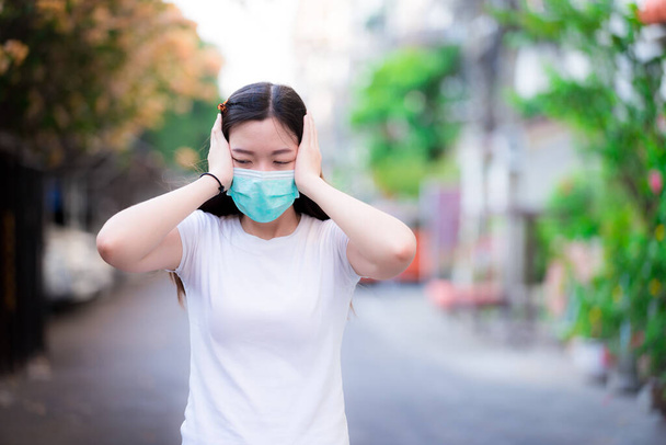Asian working women are worried and feeling stressed. She was having headaches and used her two hands to hold her temples. And she lowered her head to the floor. Young women wearing green medical mask - Φωτογραφία, εικόνα
