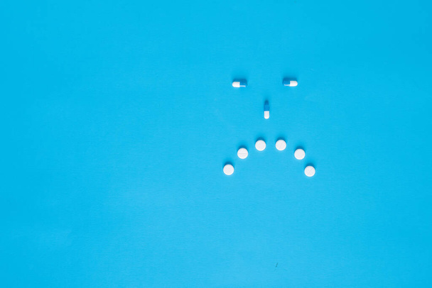  De samenstelling van tabletten en capsules op een blauwe achtergrond in de vorm van een smiley. Droevige emoties. Psychologische hulp. Kopieer de ruimte. Bovenaanzicht. Hoge kwaliteit foto - Foto, afbeelding