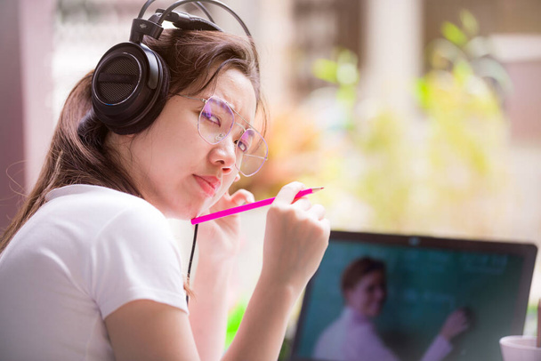 Las adolescentes están aprendiendo en línea, usando auriculares y aprendiendo de las tabletas que los maestros están enseñando. Ella hizo una cara seria y sostuvo un lápiz rosa mirando hacia atrás. - Foto, Imagen