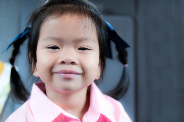 Aasialainen tyttö hymyili suloisesti. Lapsella on purkkaa silmän päässä heräämisen jälkeen. Lapsi 3-vuotias käyttää vaaleanpunaisia paitoja. - Valokuva, kuva