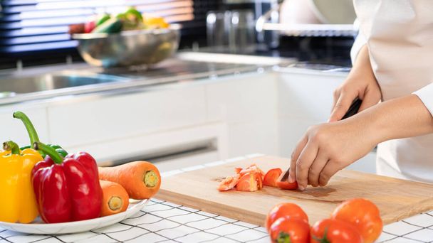 jonge Aziatische vrouw is het bereiden van gezonde voeding groente salade door Cutting tomaat voor ingrediënten op snijplank op lichte keuken, koken thuis en gezonde voeding concept - Foto, afbeelding