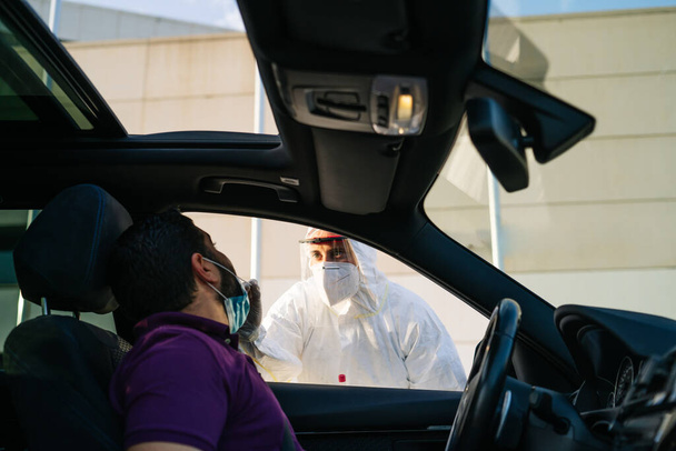 Doctor doing a PCR test COVID-19 on a patient through the car window.  - Photo, image