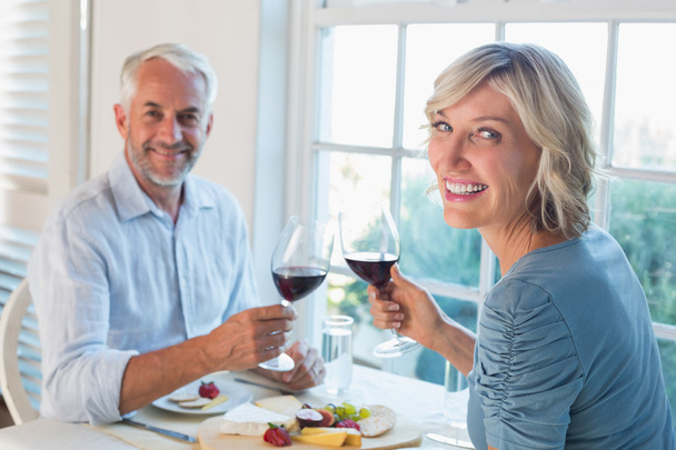 Portrait of a mature couple toasting wine glasses over food - 写真・画像