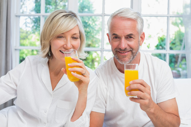 Mature couple holding orange juices at home - Фото, изображение
