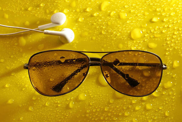 ακουστικά γυαλιά ηλίου από τον ήλιο σταγόνα νερό σε αφηρημένο κίτρινο φόντο. μελωδίες του φθινοπώρου. η έννοια των μεταβαλλόμενων εποχών - Φωτογραφία, εικόνα