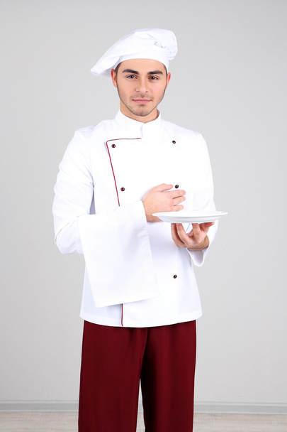 Professional chef in white uniform and hat, on gray background - Photo, image