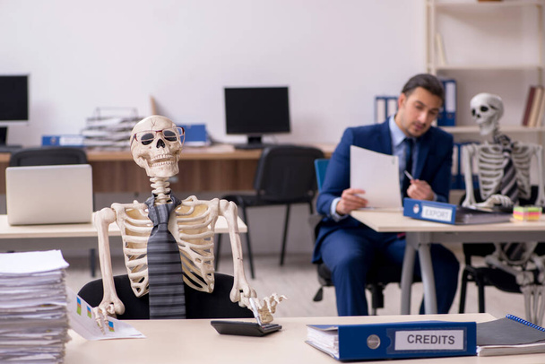 Молодой работник со скелетами в офисе - Фото, изображение