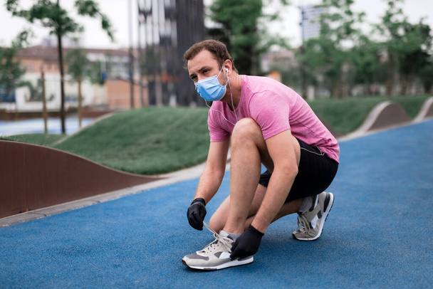 Sportivo con maschera e guanti medici, smartphone e auricolari che si allenano, facendo jogging in ambiente urbano. - Foto, immagini