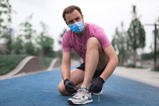 Sportsman with medical mask and gloves, smartphone and earbuds working out, jogging in urban surroundings. - Fotoğraf, Görsel
