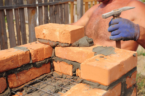 Człowiek murarz układa murowaną ścianę domu ze wzmocnioną siatką, drut za pomocą kielni i młotka murarskiego. - Zdjęcie, obraz