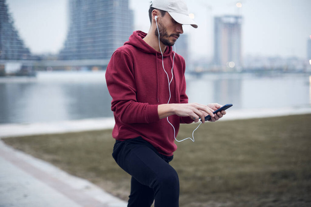Athletic sporty man training in hoodie sweatshirt in urban city park. - Fotó, kép
