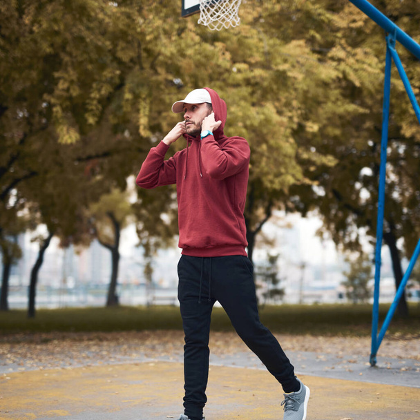 Sportos férfi tréning kapucnis pulóverben városi parkban / kosárlabda pálya. - Fotó, kép