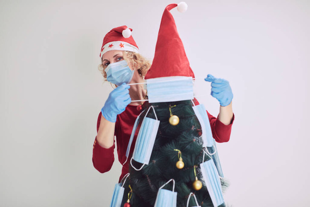 Mulher decorando árvore de Natal com máscaras médicas durante pandemia de vírus 2020 / 2021. - Foto, Imagem