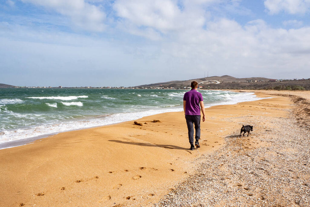 Egy férfi kutyával sétál a homokos parton, vakáció, magánélet, elszigeteltség - Fotó, kép