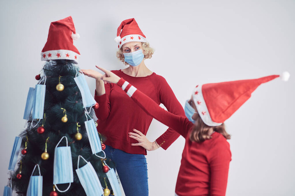 Anne ve kızı 2020 / 2021 virüs salgını sırasında tıbbi maskelerle Noel ağacını süslüyorlar.. - Fotoğraf, Görsel