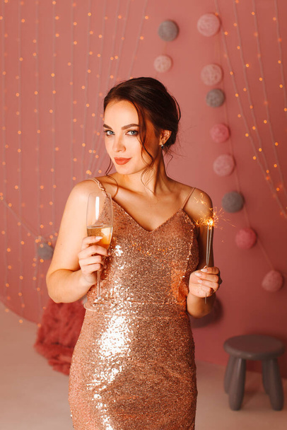 Girl in dress posing on pink background with sparklers and glass - Zdjęcie, obraz