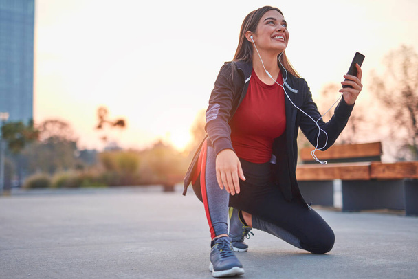Jeune femme moderne avec téléphone portable faisant une pause pendant le jogging / exercice. - Photo, image