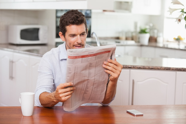 Concentrated man reading newspaper in kitchen - Foto, afbeelding