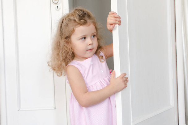 Schattig meisje gluurt uit de deur in de kamer - Foto, afbeelding