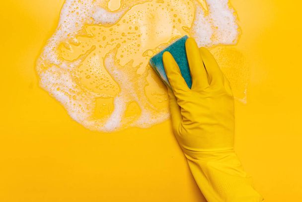  wipe the foam on a yellow background with a blue gloved sponge - Fotoğraf, Görsel