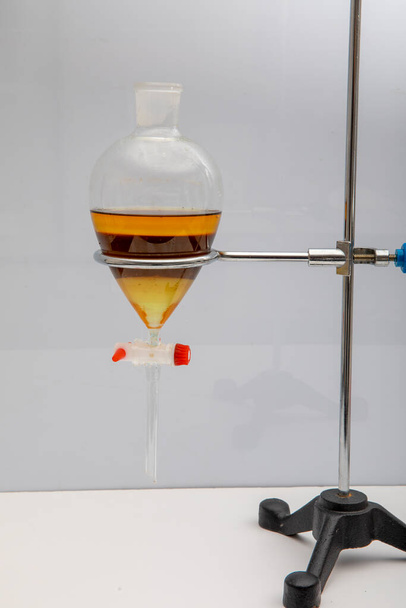 Badanie oddzielające przez filtrację substancje składowe od mieszaniny płynnej w laboratorium. Oddzielający produkt naturalny używać dichlorometan z wodą mają dwie warstwy niebieski i żółty w rozdzielaczu. - Zdjęcie, obraz