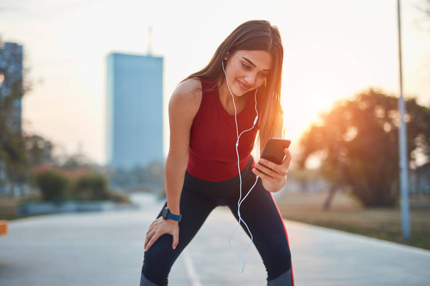 Mujer joven moderna con teléfono celular haciendo una pausa durante el jogging / ejercicio. - Foto, Imagen