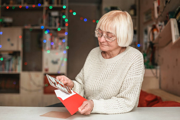 Starsza kobieta trzyma kopertę z ręcznie robioną kartką świąteczną od drogiej rodziny, opieką dziadków, świętowaniem na odległość w domu - Zdjęcie, obraz