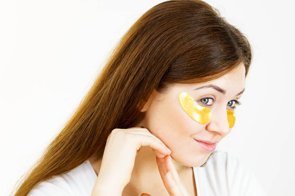 Young woman with golden collagen patches, under eye pads. Mask removing wrinkles and dark circles. Girl taking care of delicate skin around eyes. Beauty treatment. - Photo, Image
