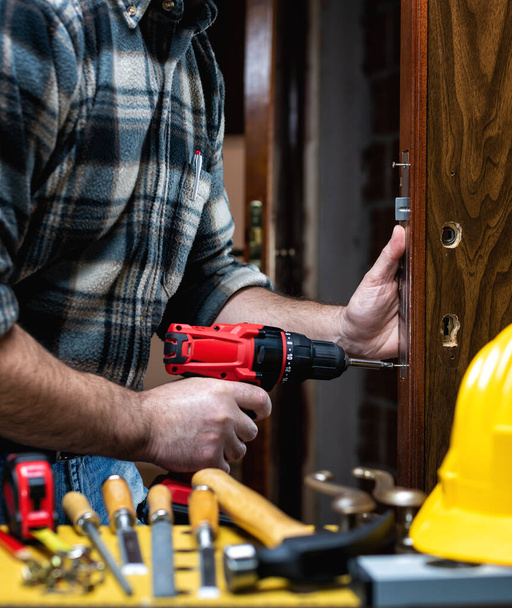 Een close-up. Timmerman met elektrische schroevendraaier bevestigt het slot van een houten deur. Bouwsector.  - Foto, afbeelding