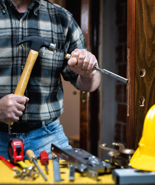 Primer plano. Carpintero con martillo y cincel prepara el agujero para la cerradura de una puerta de madera. Industria de construcción.  - Foto, imagen