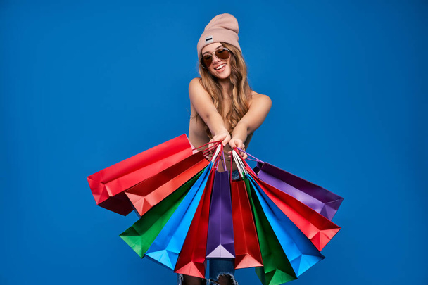 Photo of a beautiful young woman in sunglasses and a hat with packages on sale. Happy girl after shopping. - Foto, Imagen