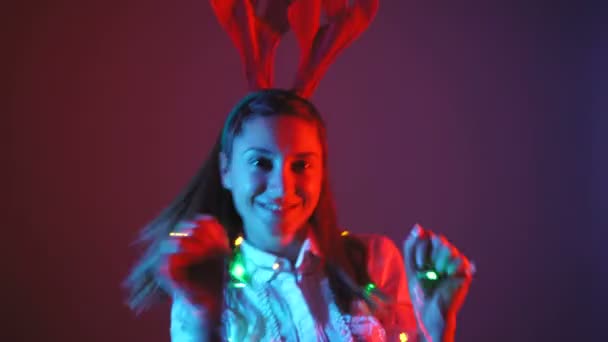 Noel dansı neon ışıkları ve geyik boynuzlarıyla çekici kadınlar. - Video, Çekim