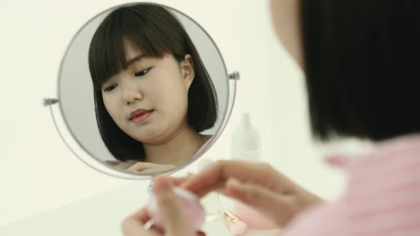 Молодая азиатская короткая прическа Боб женщина применяя крем лосьон за столом перед зеркалом. - Кадры, видео