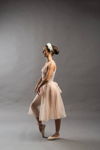 jovem bela dançarina de balé em maiô bege posando em pointes no fundo do estúdio cinza claro - Foto, Imagem