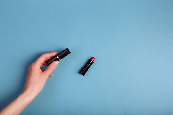 Lady's hand holding closed red lipstick isolated on blue background near to opened lipstick. - Fotografie, Obrázek