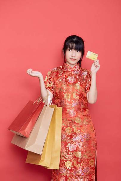 Πορτρέτο Χαριτωμένο νεαρή ασιατική γυναίκα φορούν κινέζικο φόρεμα με μια τσάντα αγορών και πιστωτική κάρτα για την κινεζική νέα χρονιά σε κόκκινο φόντο - Φωτογραφία, εικόνα