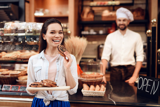 Young Smiling Woman Eating Rolls in Modern Bakery. - Foto, Bild