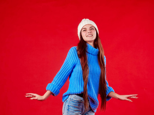  beautiful girl in a sweater and a hat on a red background - Zdjęcie, obraz