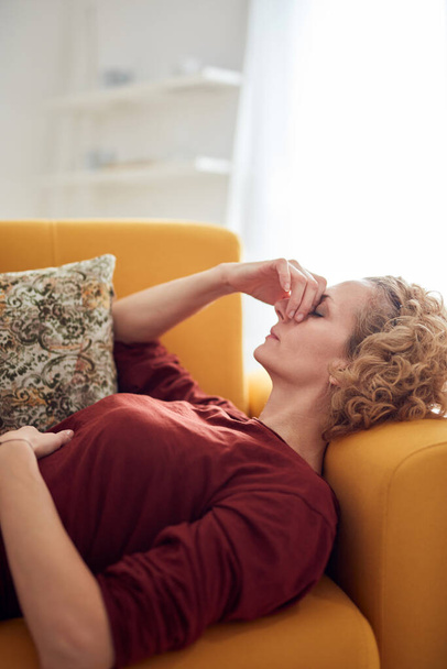 Mujer con dolor sinusal, dolor de cabeza y problemas de estómago, acostada en un sofá en casa. - Foto, Imagen