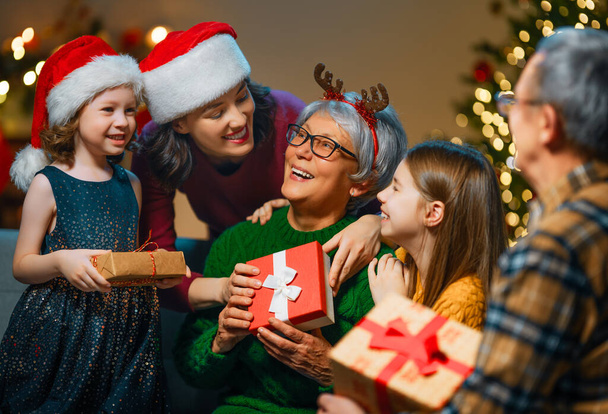 Merry Christmas and Happy Holidays! Grandma, grandpa, mum and children exchanging gifts. Parents and daughters having fun near tree indoors. Loving family with presents in room. - Foto, imagen