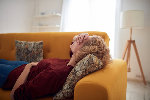Γυναίκα με φλεβοκομβικό άλγος, πονοκέφαλο και στομαχικά προβλήματα, ξαπλωμένη σε καναπέ στο σπίτι. - Φωτογραφία, εικόνα