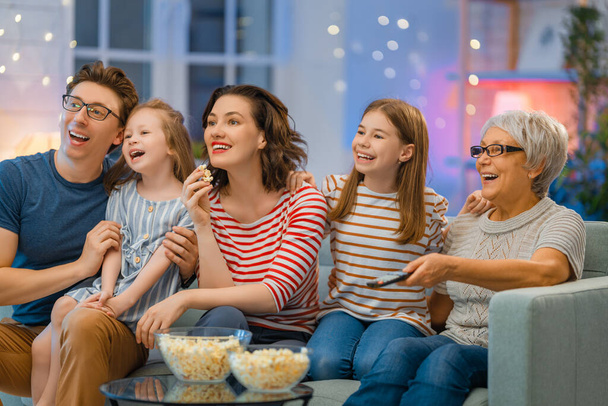 Happy family watching projector, TV, movies with popcorn in the evening at home. Granny, mother, father and daughters spending time together. - Valokuva, kuva