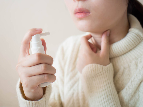 Sick woman using spray medication for relief of painful sore throats, cough, pharyngitis and hoarseness. Pharmaceutical product. Health care and medical concept. Close up. - 写真・画像